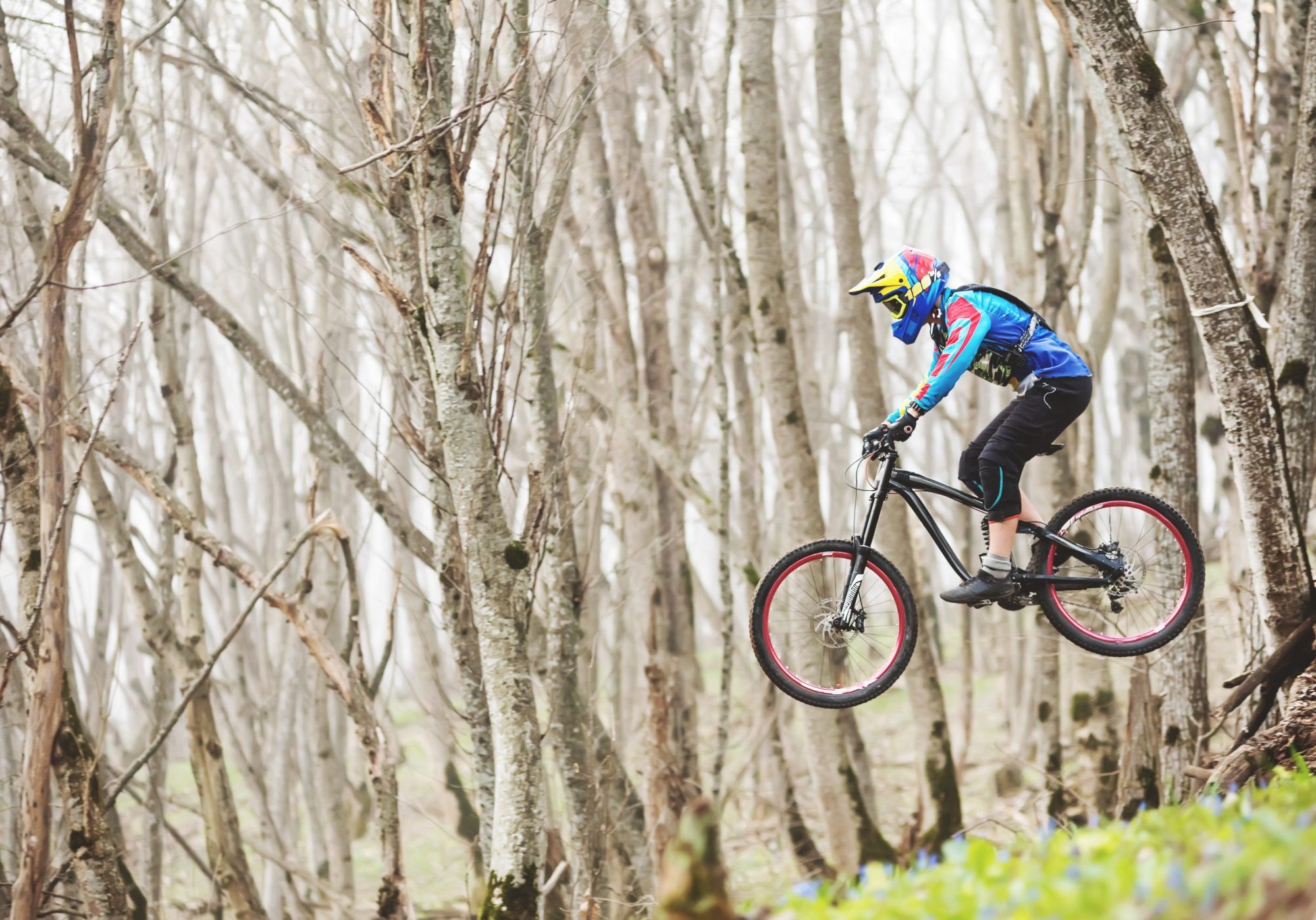 A mountain bike rider jumps from a springboard in a foggy forest.